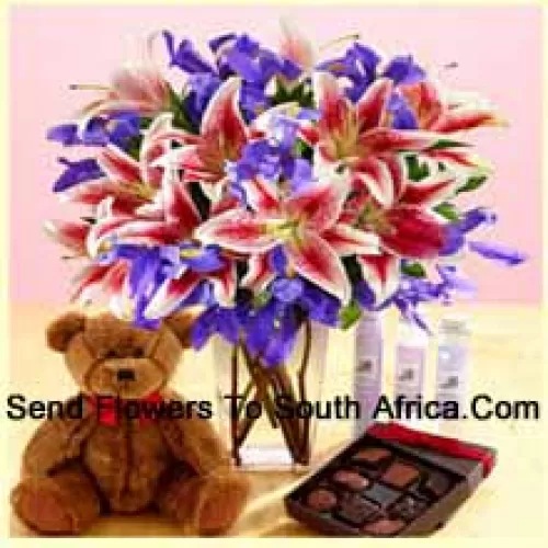 الزنابق الوردية والزهور البنفسجية المتنوعة مرتبة بشكل جميل في مزهرية زجاجية ، دمية دب براون طولها 12 بوصة وصندوق مستورد من الشوكولاتة