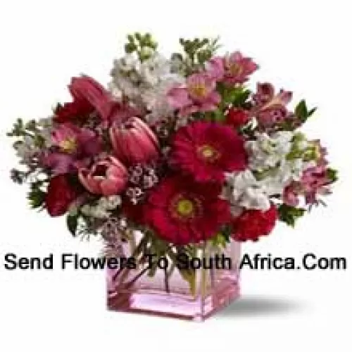 Roses rouges, tulipes rouges et fleurs assorties avec des remplisseurs saisonniers arrangés magnifiquement dans un vase en verre