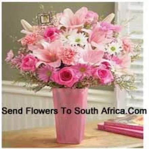 Roses roses, oeillets roses, gerberas roses, gerberas blancs et lys roses avec des remplissages saisonniers dans un vase en verre